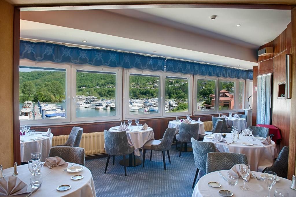 A restaurant with tables set for dining, large windows with a view of boats and greenery.