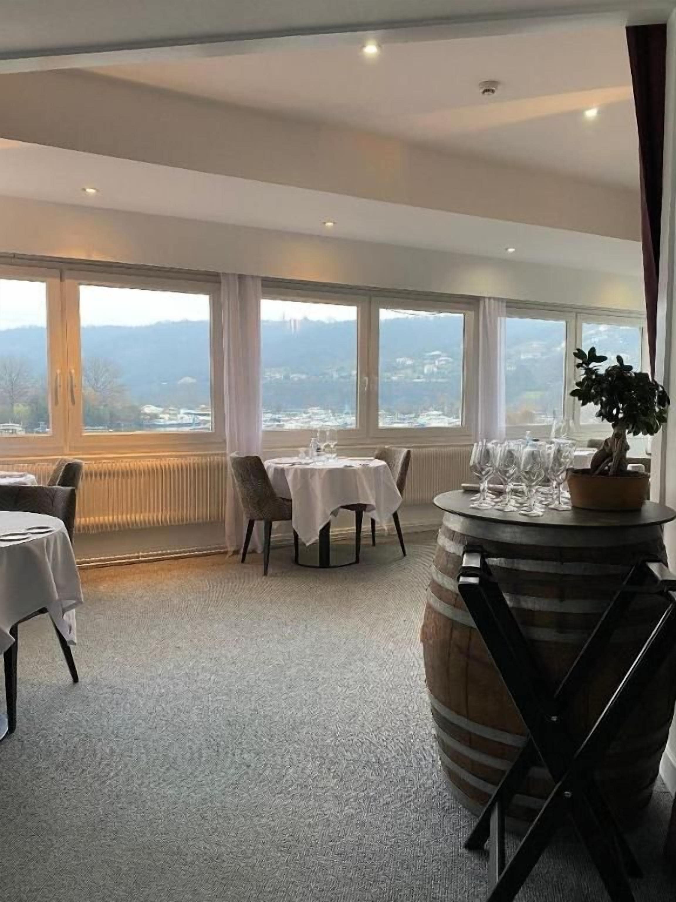 Un comedor con mesas y sillas, un barril grande y vistas del paisaje a través de amplios ventanales.