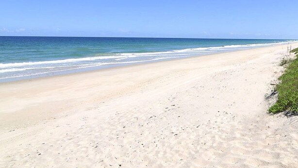 A wide sandy beach with gentle waves, a clear sky, and a distant horizon. - Avis House (Palm Bay)