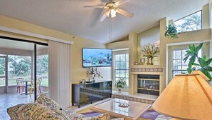 A spacious living room with a ceiling fan, a fireplace, a TV, and a large window. - Avis House (Palm Bay)