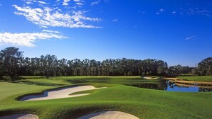A golf course with sand bunkers, a pond, and a line of trees under a clear sky. - Avis House (Palm Bay)
