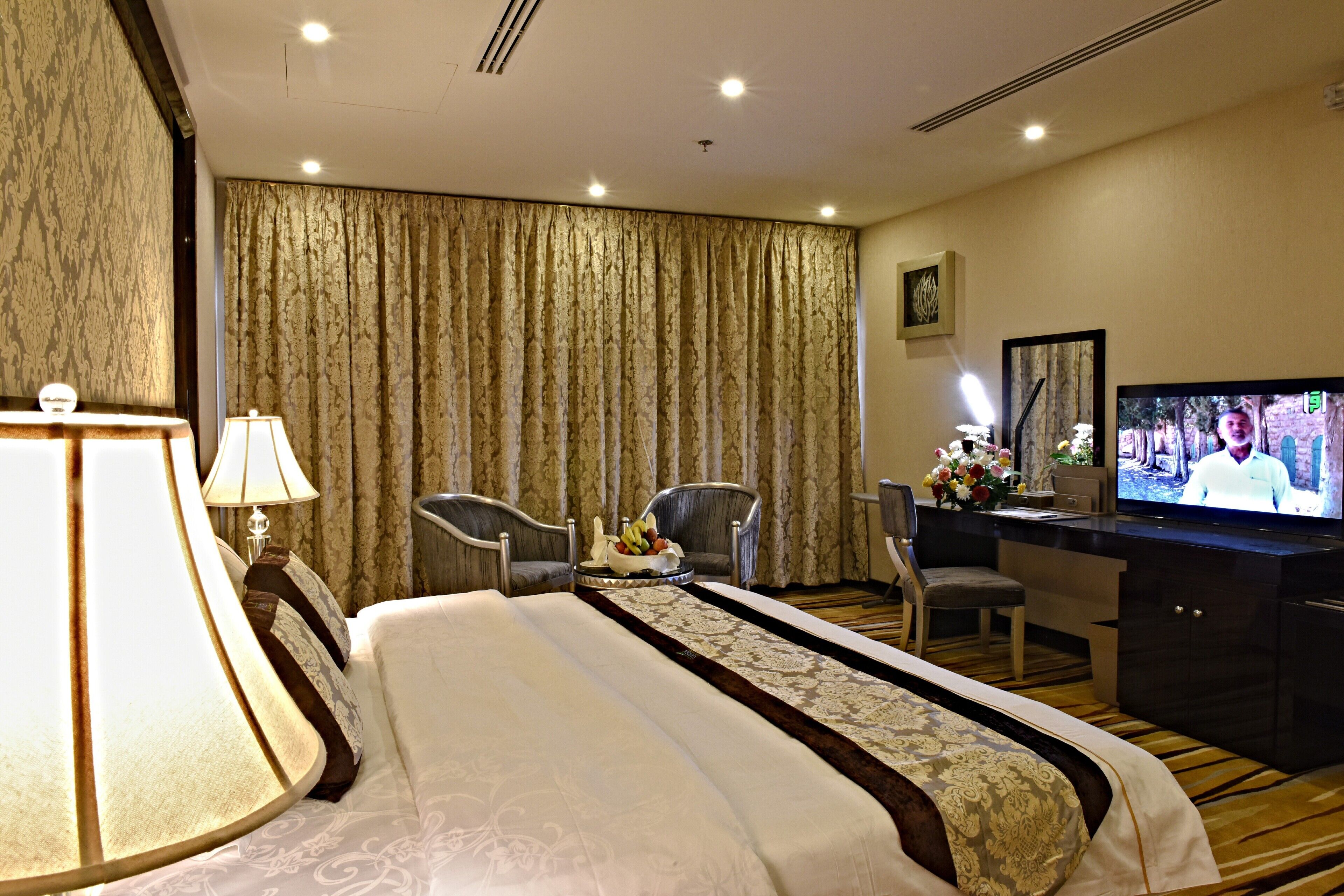 A hotel room with a large bed, two chairs, a desk with a TV, and a curtain.