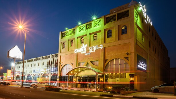 Un hotel con un letrero llamativo que dice 'Garden Plaza Hotel' y una amplia entrada con porche cubierto.