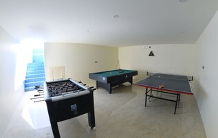 A room with a foosball table, pool table, and a staircase with blue tiles.