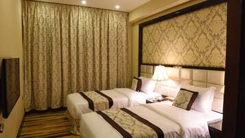 A hotel room with two beds, a headboard, a bedside table with a lamp, and a large window with curtains.