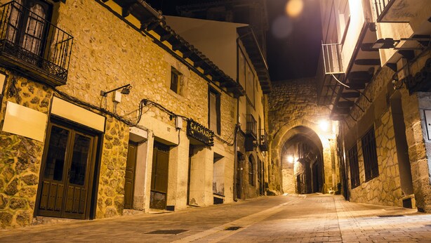 Una calle estrecha con edificios de piedra, arcos y balcones.