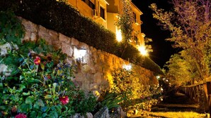 Una pared de piedra con una lámpara y una escalera que sube hacia un edificio de noche.