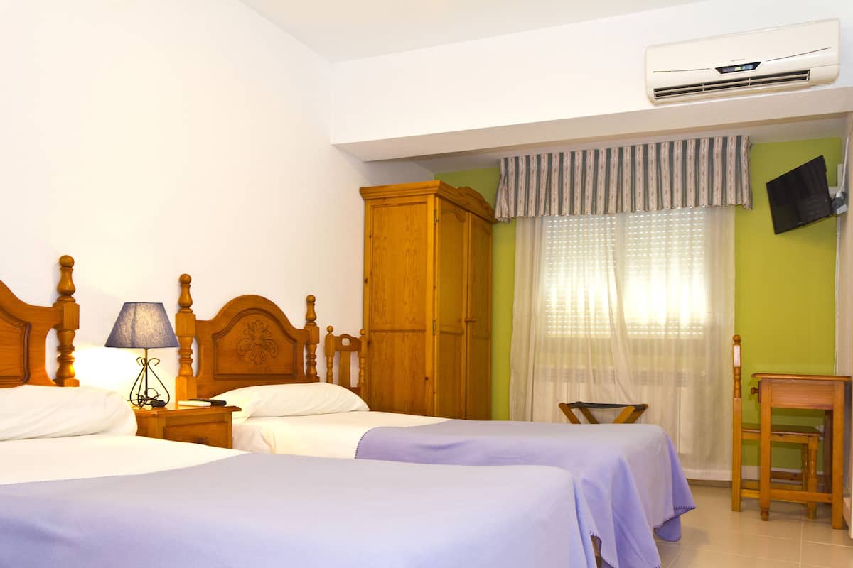 Habitación de hotel con dos camas, un armario de madera, una mesa, una silla, aire acondicionado y un televisor fijado a la pared.