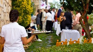 Una persona sosteniendo una bandeja de comida en un evento al aire libre con mesas e invitados.