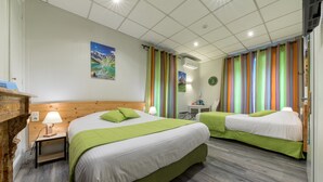 Une chambre d’hôtel avec deux lits, une tête de lit en bois, une table de chevet avec une lampe, une petite table avec une lampe et des rideaux colorés.