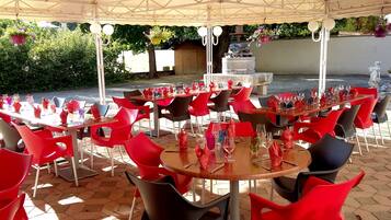 Un área de comedor al aire libre con mesas y sillas, una fuente y follaje de fondo.