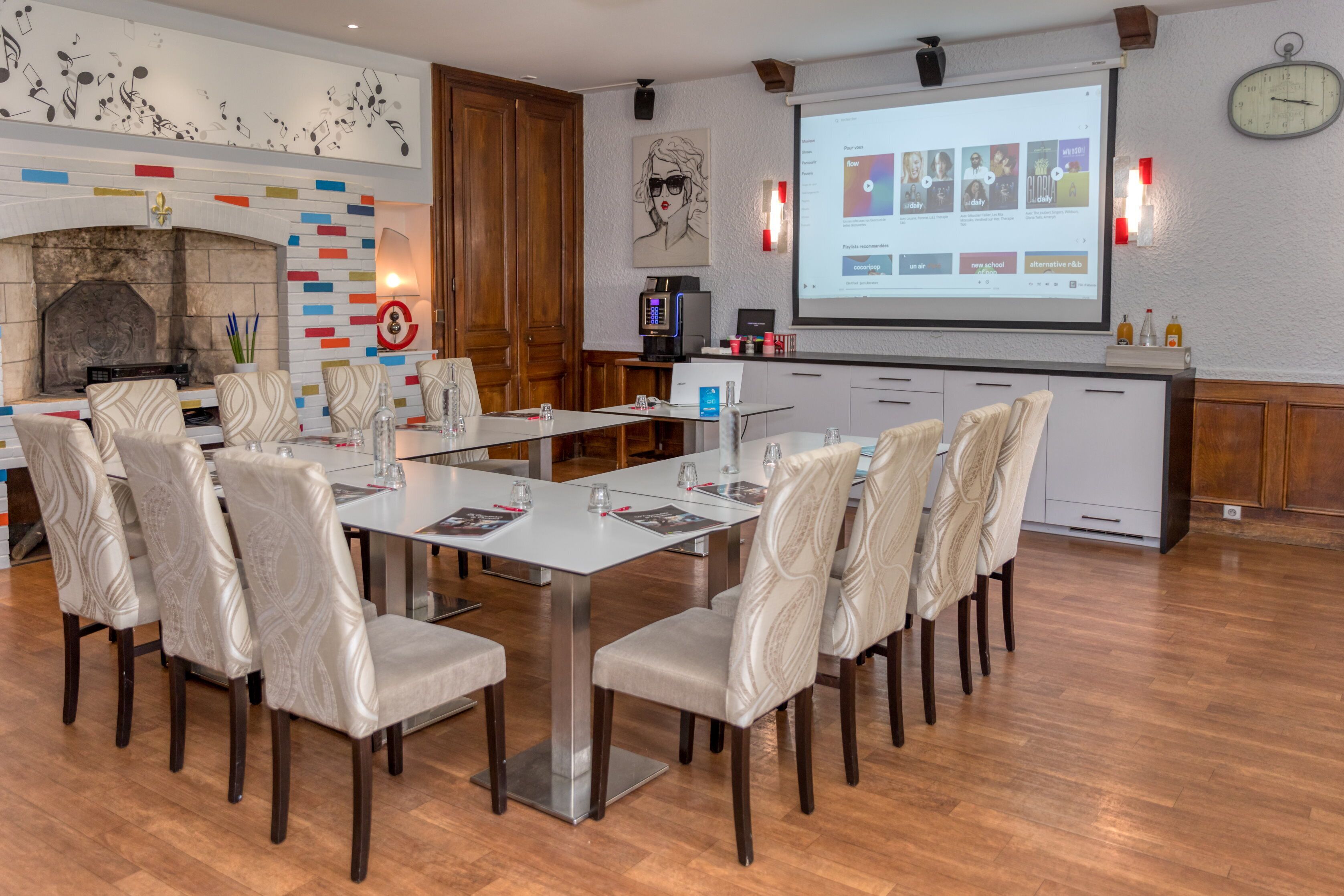 A conference room with a long table, chairs, a fireplace, a projector screen, and a clock on the wall.