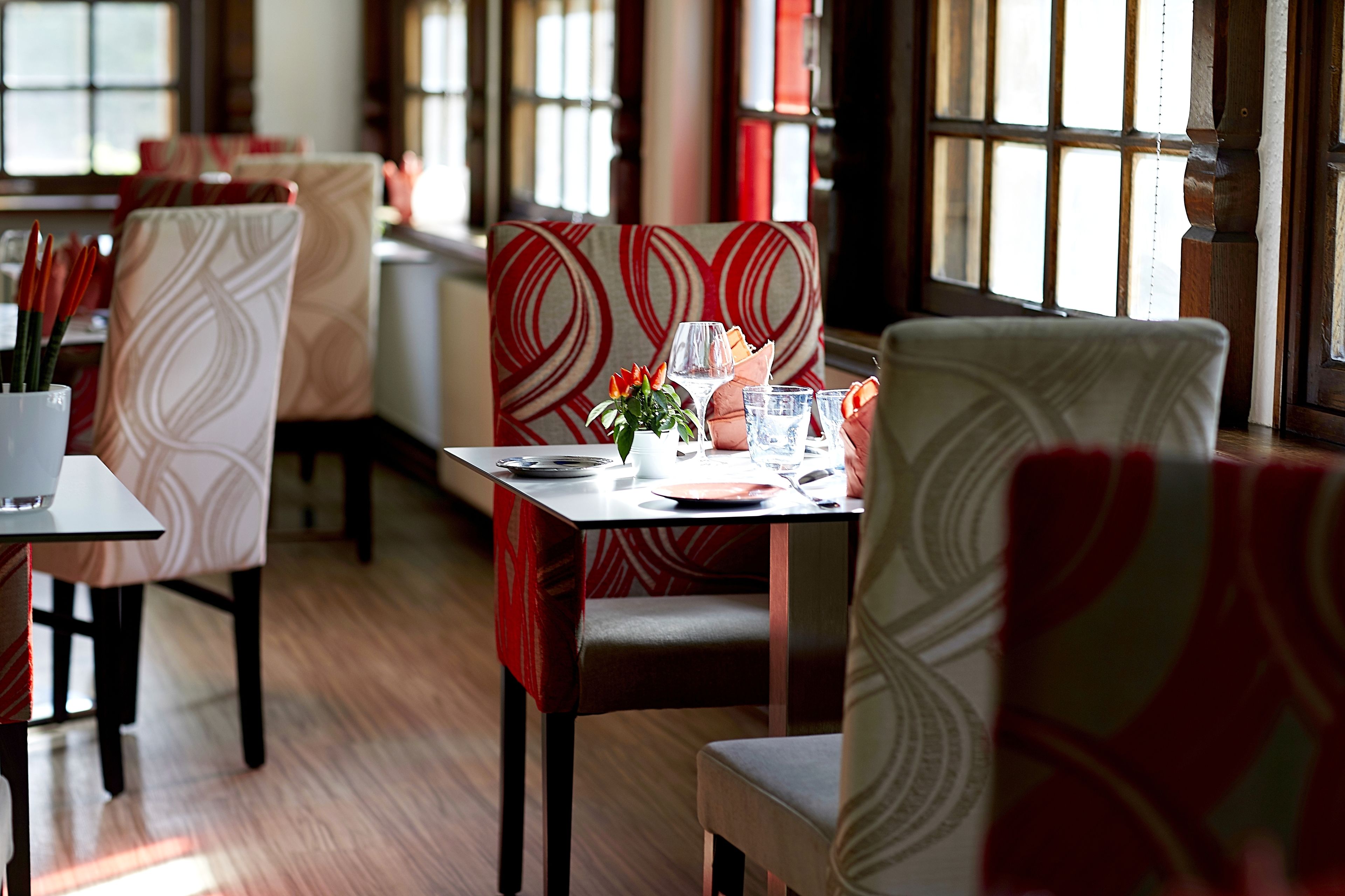 Interior de un restaurante con sillas y mesas estampadas, ventanas amplias y suelo de madera.
