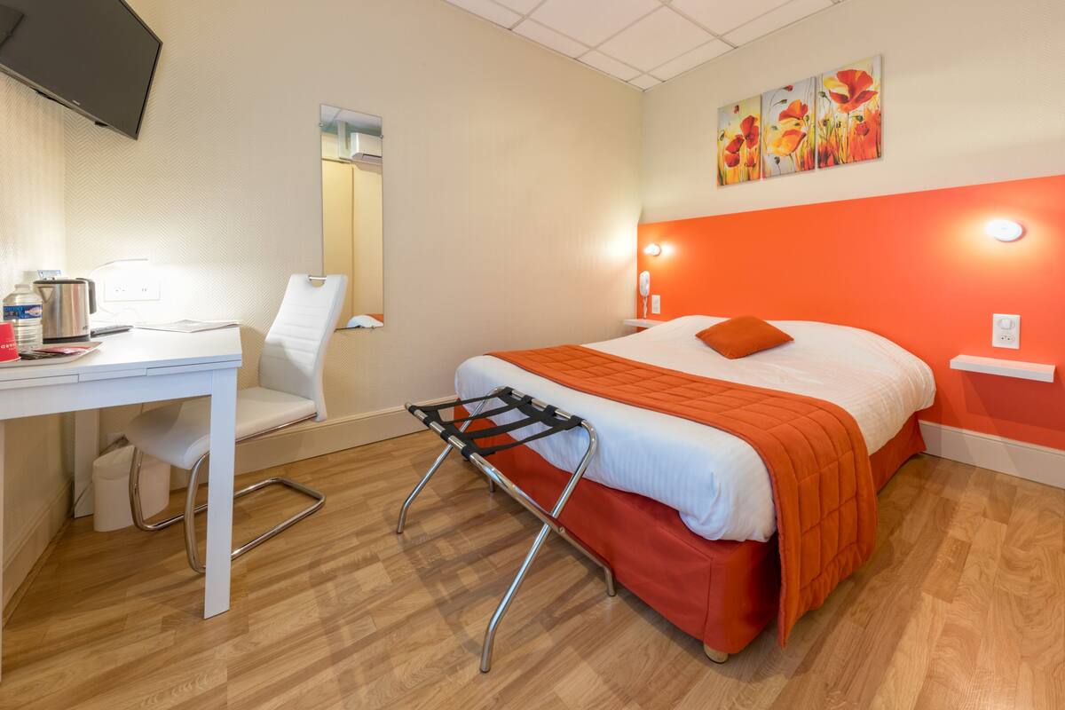 Habitación de hotel con cama, escritorio, silla, espejo y un cuadro en la pared.
