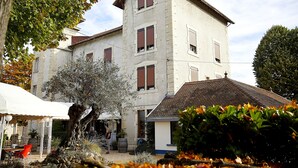 Un immeuble à plusieurs étages, doté d’une façade en pierre, d’un toit recouvert de tuiles et d’un espace jardin aménagé avec des sièges extérieurs.