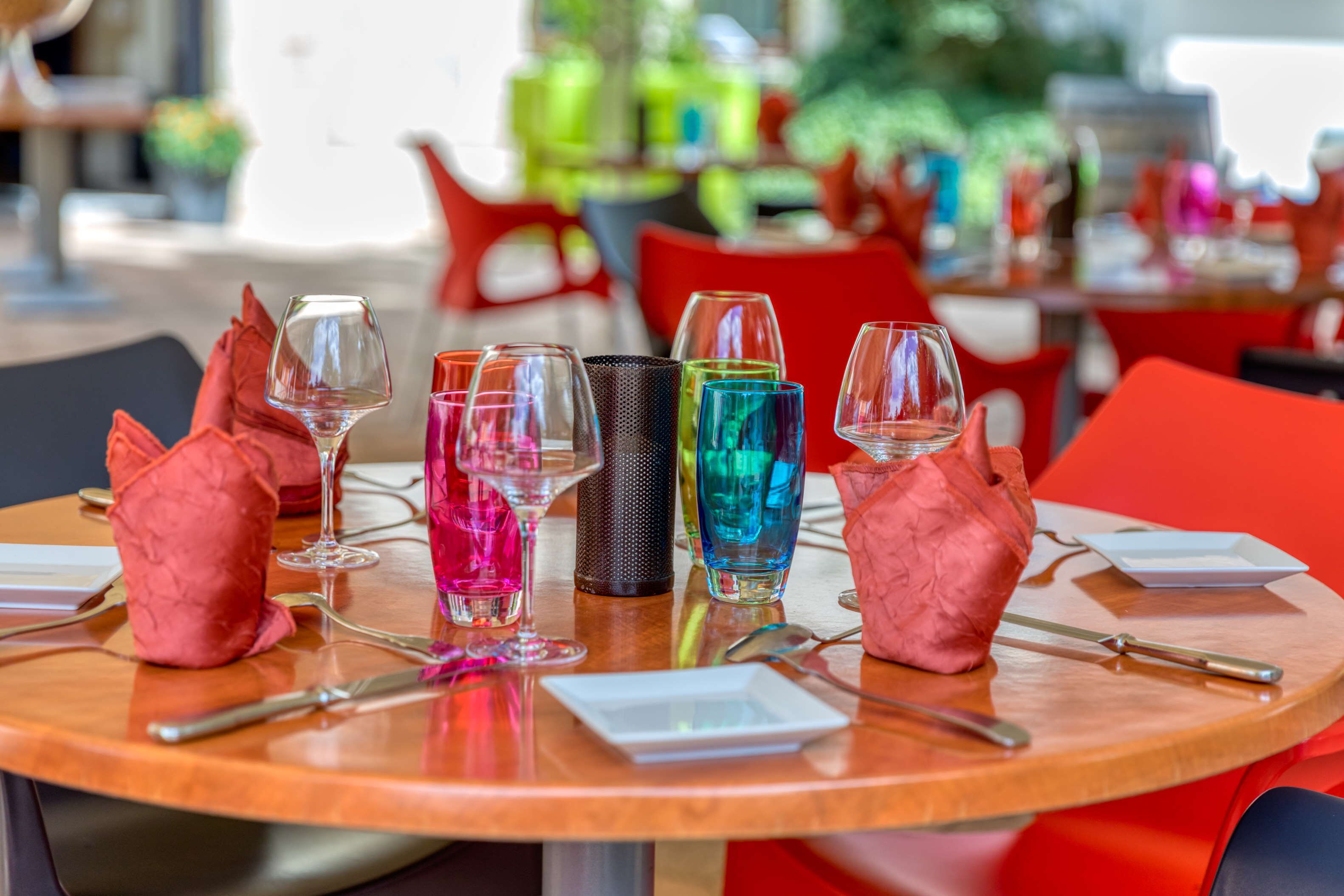Una mesa redonda con varios vasos de colores y algunos adornos rojos.