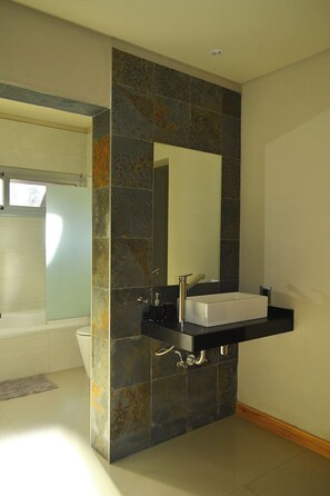 Un baño moderno con un lavamanos independiente, un espejo grande y una zona de ducha.