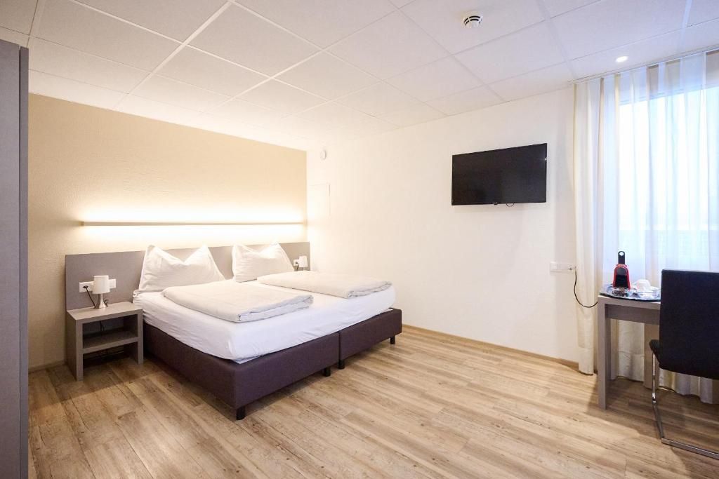 Een hotelkamer met een bed, nachtkastje, lamp, televisie, bureau, stoel en een raam met gordijnen.