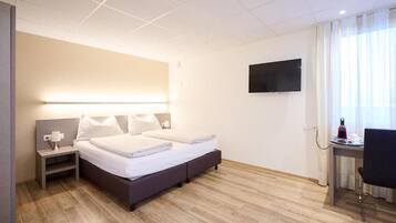 Een hotelkamer met een bed, nachtkastje, lamp, televisie, bureau, stoel en een raam met gordijnen.