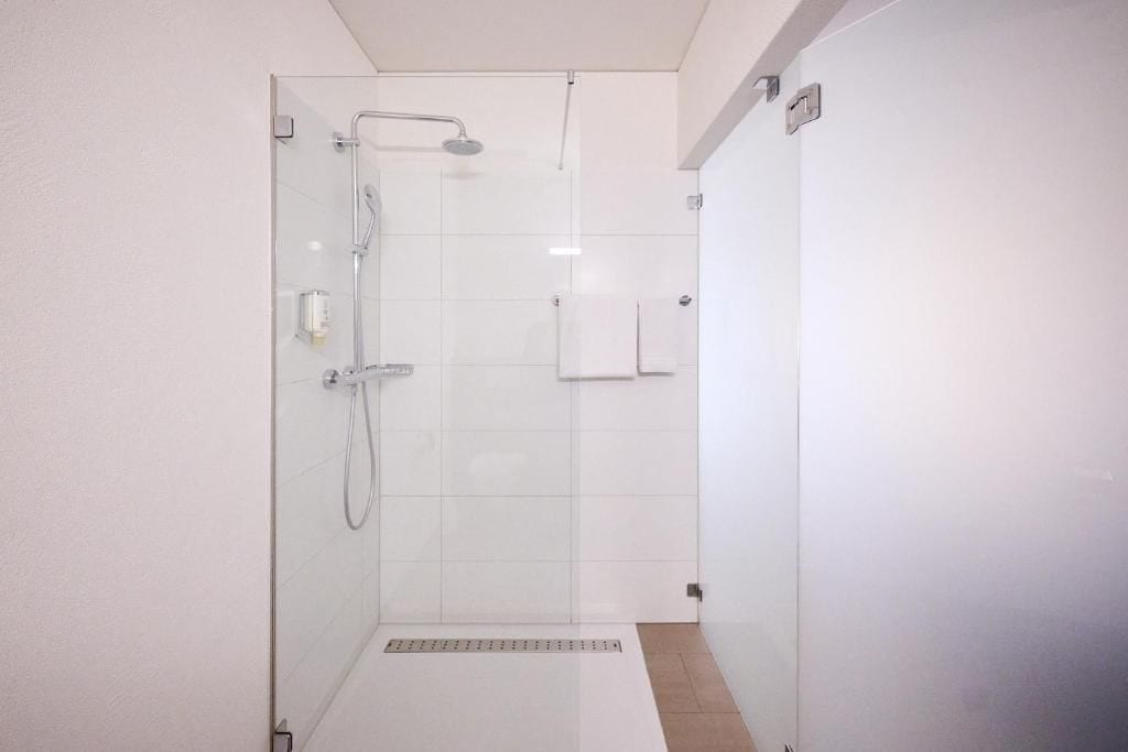 Un área de ducha con paredes de vidrio, un cabezal de ducha de mano y un grifo empotrado en la pared.