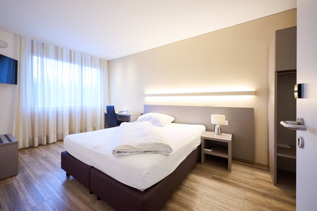 A modern hotel room with a large bed, bedside tables, a desk, and a TV mounted on the wall.