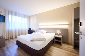 A modern hotel room with a large bed, bedside tables, a desk, and a TV mounted on the wall. - Smart Hotel Kreisel -- Self Check-in (Lachen)