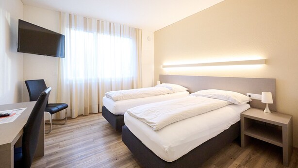 Habitació d'hotel amb dos llits, un escriptori, una cadira, un televisor i una taula de nit amb una làmpada.