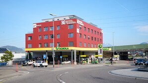 Un edifici vermell de diversos pisos, amb una secció inferior groga i indicadors que diuen "AGROLA" i "HOTEL KRIESEL".