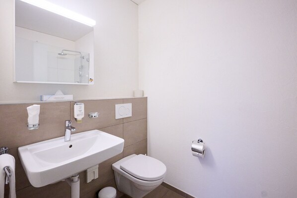 A modern bathroom with a white sink, mirror, and toilet. - Smart Hotel Kreisel -- Self Check-in (Lachen)