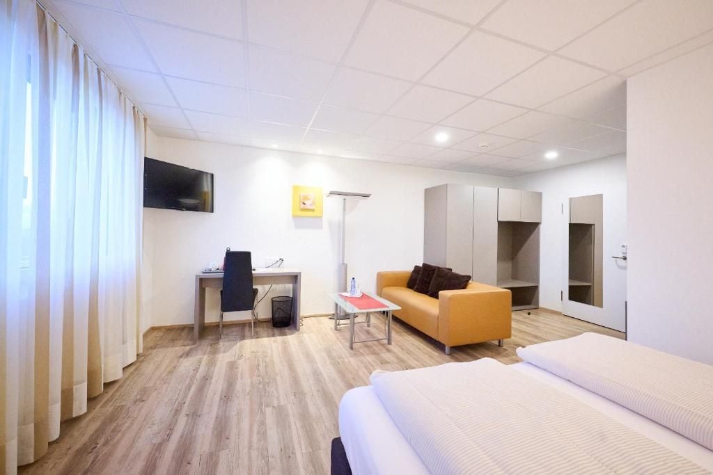 Habitación de hotel con cama, escritorio, silla, sofá, televisión y armario.