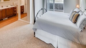 A bedroom with a large bed, a bathroom with wooden cabinets, and a view of the outdoors. - Beachwood Estate (Ocean Park)