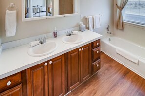 A bathroom with two sinks, a mirror, a bathtub, wooden cabinets, and a window with curtains. - Beachwood Estate (Ocean Park)