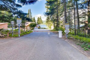 A gated entrance with multiple warning signs, a clear road leading to a building, and a natural landscape with trees and a lake in the background.