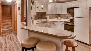 A modern kitchen with white cabinets, a large island with stools, a built-in oven, and a hanging light fixture.
