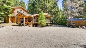 A wooden cabin with a porch, a covered deck, and a gravel driveway.