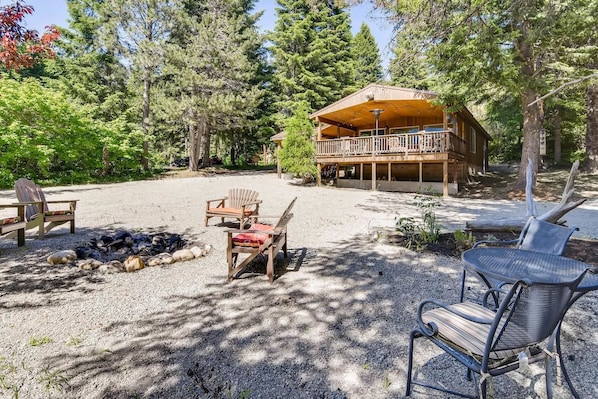 A cabin with a deck, surrounded by trees, and equipped with outdoor seating and a fire pit.