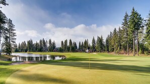 A golf course with a pond, surrounded by tall pine trees and a lodge.