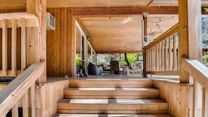A wooden staircase leading to an outdoor deck with a covered area, featuring a view of outdoor furniture and a sign.