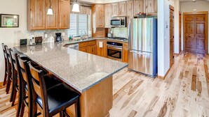 A kitchen with wooden cabinets, a granite countertop, stainless steel appliances, and a bar seating area. - Cascade Mountain Villa (Cle Elum)