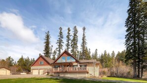 A two-story house with a large deck, surrounded by tall trees and a clear sky. - Cascade Mountain Villa (Cle Elum)