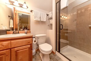 A bathroom with a wooden vanity, a toilet, a glass-enclosed shower, and a mirror with lights.