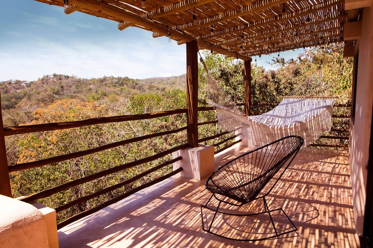 A balcony with a hammock, a chair, and a view of a hilly landscape.