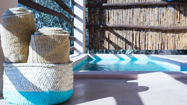 A pool area with a bamboo fence and a woven basket with towels. - Casa Mono (Santa María Tonameca)