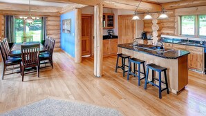A spacious kitchen with wooden cabinetry, a central island with stools, and a dining area with a table and chairs.