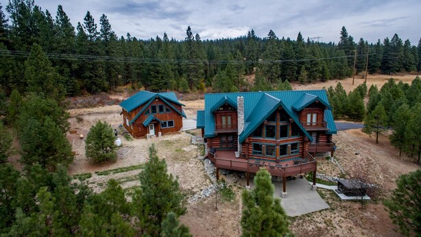 A cabin with a large deck and a separate garage, surrounded by dense forest.