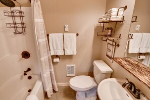 A bathroom with a toilet, sink, and shower area. There are towels hanging on the wall and a towel rack. - Elk Run Chalet (Cle Elum)