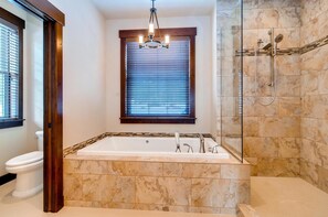 A modern bathroom with a freestanding bathtub, a glass-enclosed shower, and a window with blinds. - Elk Run Lodge (Cle Elum)