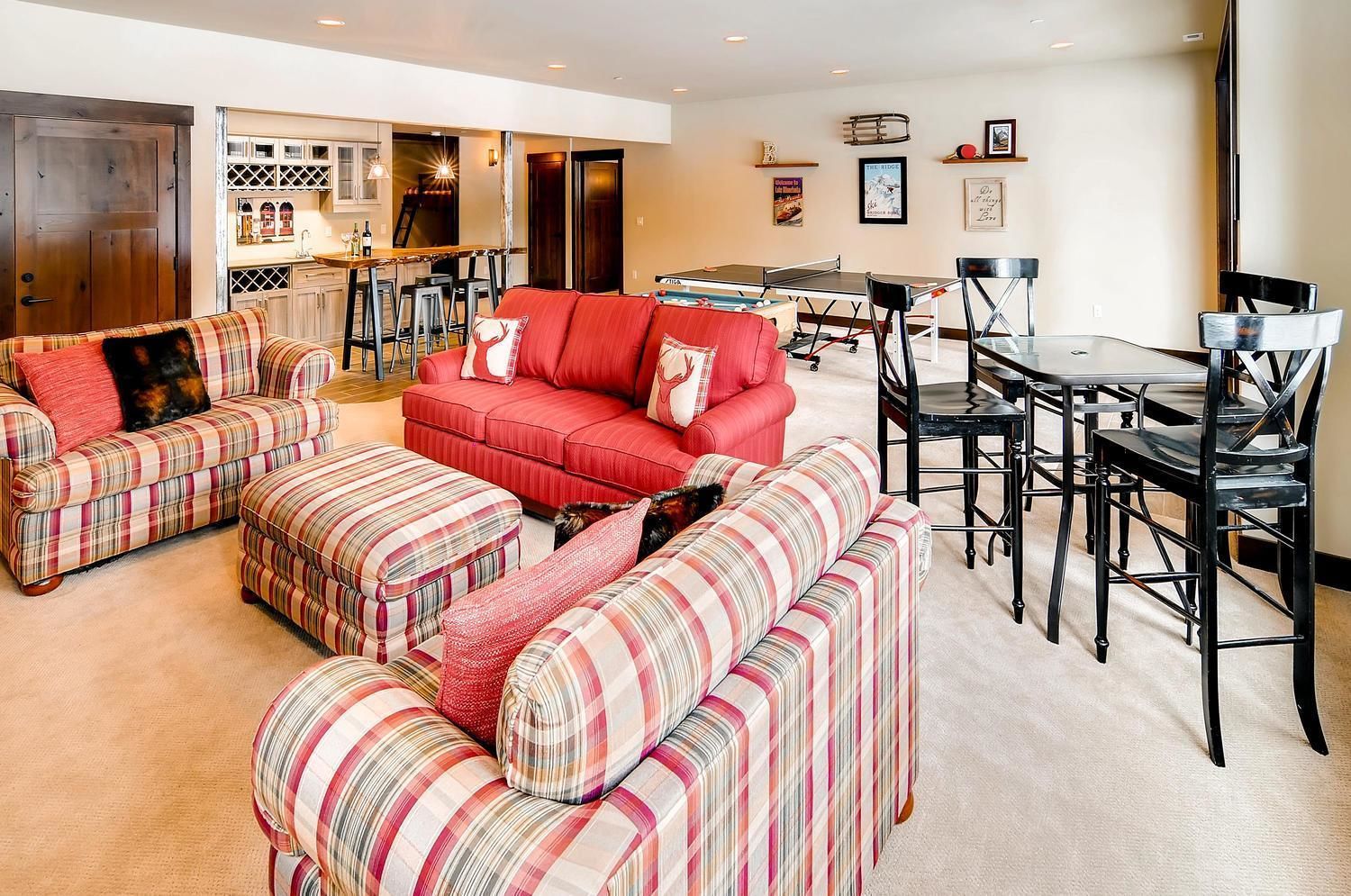 A spacious living room with a red sofa, striped ottomans, and a dining area with a table and chairs.