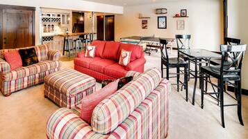 A spacious living room with a red sofa, striped ottomans, and a dining area with a table and chairs.
