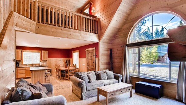 Interior acogedor de una cabaña con comedor, sala de estar con sofá y mesa de centro, y un amplio ventanal con vistas al exterior.